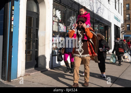 A busy street scene on 37th Avenue in Jackson Heights featuring a father carrying his daughter on his shoulders. In Queens, New York City. Stock Photo