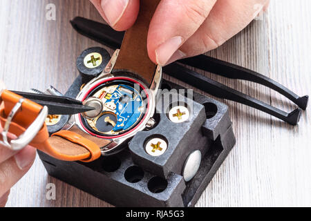 watch repairer workshop - watchmaker replaces battery in quartz wristwatch with plastic tweezers on wooden table close up Stock Photo