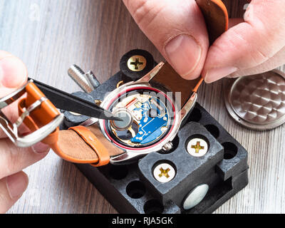 watch repairer workshop - watchmaker repairs quartz wristwatch with plastic tweezers on wooden table close up Stock Photo