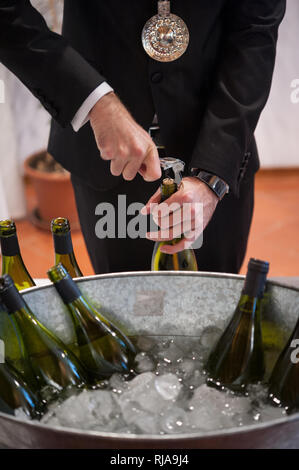 Sommelier is opening wine bottle with corkscrew. Big metal ice bucket with bottles in the foreground. Stock Photo