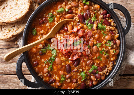 American cowboy beans with ground beef, bacon in a spicy sauce close-up on the table. horizontal top view from above Stock Photo