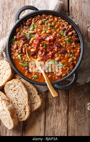 Delicious cowboy stew of beans with ground beef, bacon in a spicy sauce closeup in a bowl on the table. Vertical top view from above Stock Photo