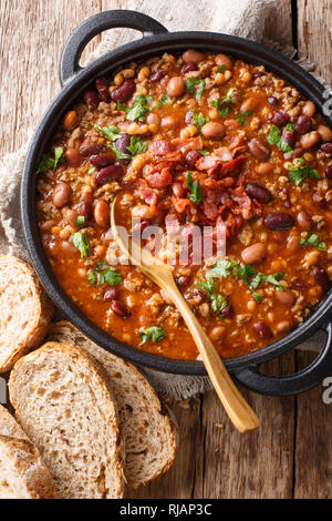 Crock pot beans with ground beef, bacon in a spicy sauce closeup in a bowl on the table. Vertical top view from above Stock Photo