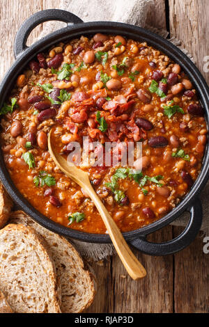 American cowboy beans with ground beef, bacon in a spicy sauce close-up on the table. Vertical top view from above Stock Photo