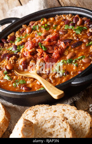 American cowboy beans with ground beef, bacon in a spicy sauce close-up on the table. vertical Stock Photo