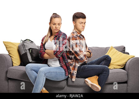 Teenage boy and girl sitting on a sofa angry with each other isolated on white background