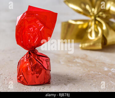 A cherry chocolate bonbon wrapped in red paper with a golden bow tie ribbon in the background. Stock Photo