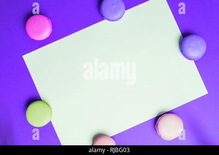 Closeup paper for copy space, text and advertising on purple background with multicolored pink and yellow macaroons. Frame and form for copy space Stock Photo