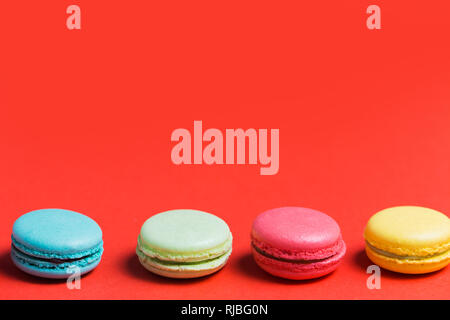Sweet and colourful french macaroons or macaron on red background with copy space. Dessert, homemade cake Stock Photo