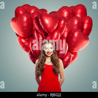 Girl in red dress with heart balloons. Beautiful woman with red lips makeup, perfect curly hair and cute smile. Surprise, valentines people and Valent Stock Photo