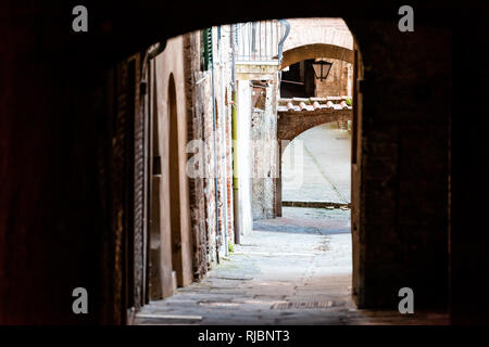 Siena, Italy dark narrow alley street in historic medieval old town village in Tuscany with nobody and arch tunnel passage Stock Photo
