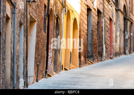 Siena, Italy narrow steep alley street in historic medieval old town village in Tuscany with nobody during summer day and yellow colorful architecture Stock Photo