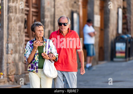 San Gimignano, Italy - August 27, 2018: People senior couple walking exploring small historic medieval town village in Tuscany during sunny summer day Stock Photo