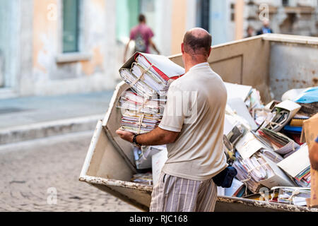 Perugia, Italy - August 29, 2018: Italian street outside in city sunny day with man throwing away books and documents papers on garbage truck Stock Photo