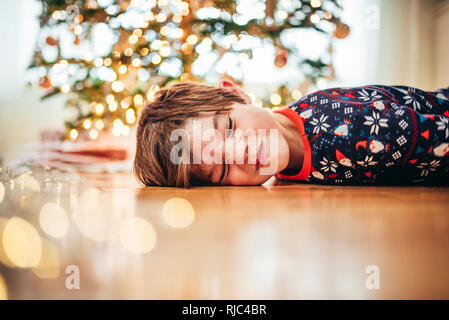 Boy lying on the floor in front of a Christmas tree pulling funny faces Stock Photo