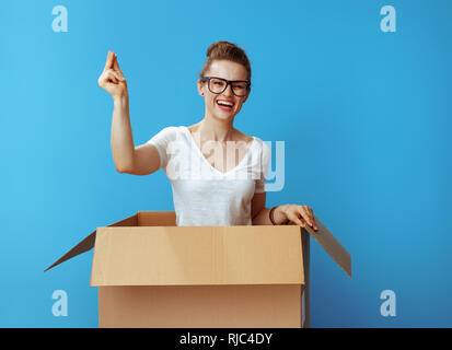 happy modern woman in white t-shirt with fingers snapping in a cardboard box isolated on blue background Stock Photo
