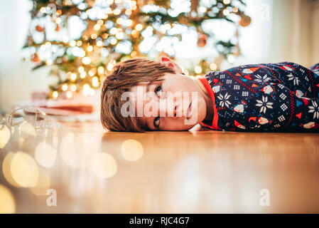Boy lying on the floor in front of a Christmas tree pulling funny faces Stock Photo