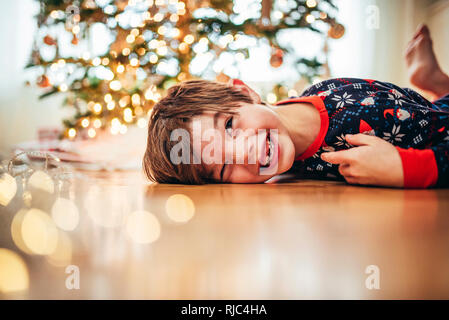 Boy lying on the floor in front of a Christmas tree laughing Stock Photo