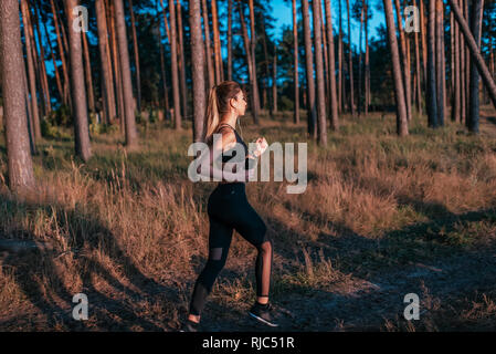 Beautiful girl in sportswear running on a run. Woman in the summer in forest. With headphones listening to music motivates yourself. The concept of a Stock Photo