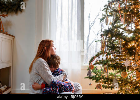 Woman sitting by a Christmas tree hugging her son Stock Photo