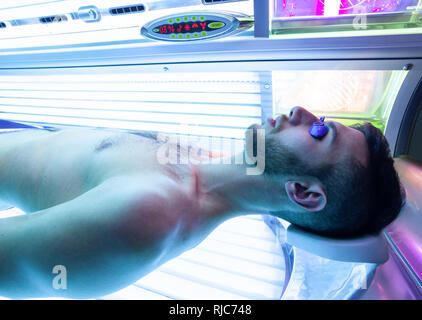 Young Thin Man At Solarium In Beauty Salon. Full tanning bed. Stock Photo