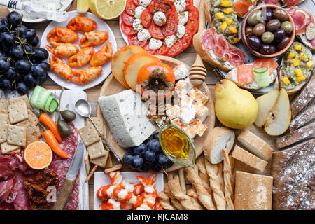 Italian antipasti snacks set. Brushettas, cheese variety, shrimps, salmon, olives, prosciutto with pear, salami and jamon over grey grunge table, top view. Food photography Stock Photo