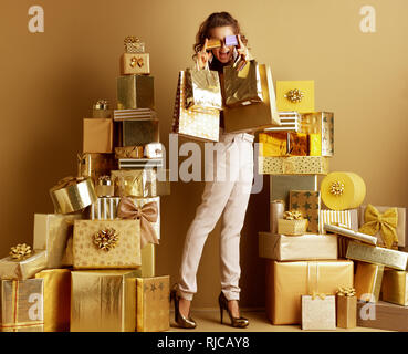 Full length portrait of happy young woman in gold beige pants and brown blouse with shopping bags holding 2 credit cards in the front of eyes among 2  Stock Photo