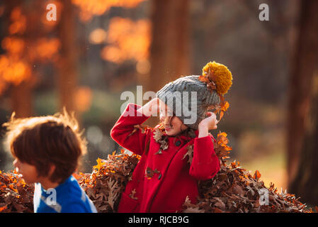 Boy and girl playing in a pile of leaves, United States Stock Photo