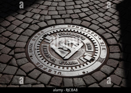 Cast iron manhole cover on a cobblestone street in a city of Stavanger, Rogaland county, Norway, Scandinavia Stock Photo