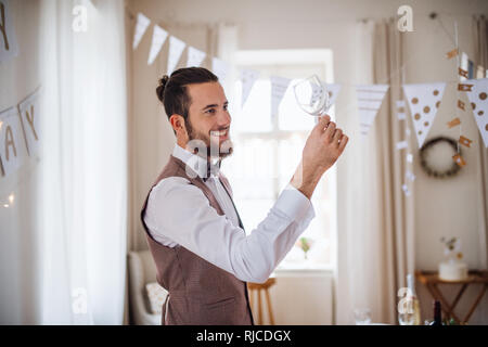 A portrait of young man indoors in a room set for a party, looking at wine glass. Stock Photo