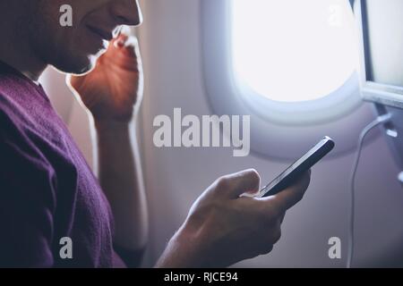 Connection during flight. Young man using mobile phone in airplane. Stock Photo