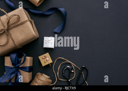 Creative gift boxes on dark background. Wrapping with brown paper, ribbon and scissors Stock Photo
