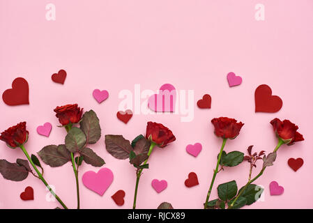 True love. Red roses with decorative paper hearts on pink background. Top view Stock Photo