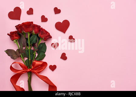 True love. Bouquet of roses with red ribbon for her with decorative paper hearts on pink background Stock Photo