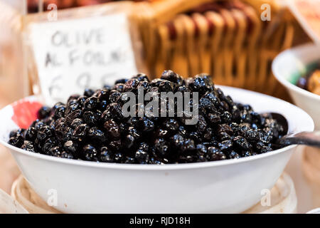 Black olives many closeup in Florence Italy central market in bowl with sign and spoon scoop Stock Photo