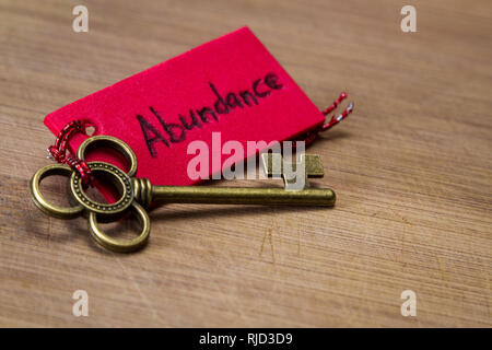 concept image using a key and a tag with the word abundance handwritten on it over a wooden background Stock Photo