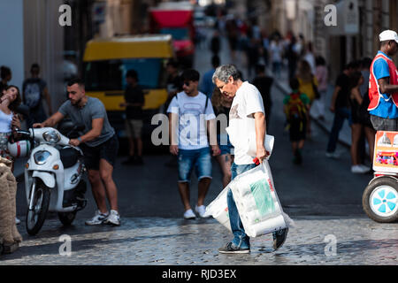 Rome, Italy - September 4, 2018: Local Italian Roma man male walking carrying grocery bags with toilet paper crossing street road busy sidewalk and ma Stock Photo