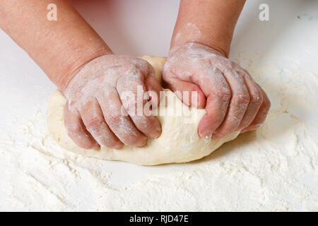 Senior woman kneads raw fresh dough with hands on the table. Stock Photo