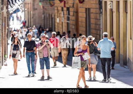 Siena, Italy - August 27, 2018: Street in historic medieval old town village in Tuscany with crowd of many people tourists walking during sunny summer Stock Photo