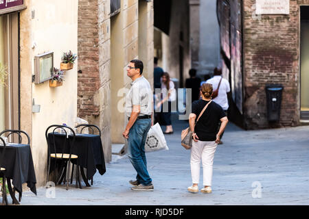 Siena, Italy - August 27, 2018: Alley street in historic medieval old town village in Tuscany with tourists people copule looking reading menu of cafe Stock Photo