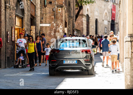 Siena, Italy - August 27, 2018: Street in historic medieval old town village in Tuscany with many people tourists walking and car on narrow alley Stock Photo