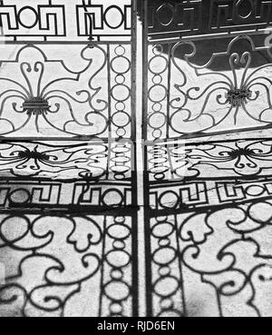 Closed iron crafted gate giving shadows on a grey floor, seen in Cuyo Town, Philippines. Photo is in black and white. Stock Photo