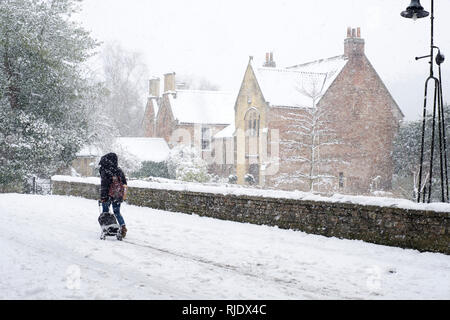 Lady pulling shopping trolley on snow covered St. Andrew's Street in Wells, Somerset, UK Stock Photo