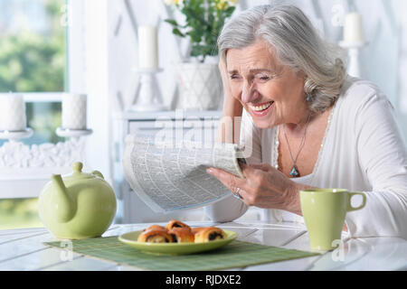 Portrait of senior woman reading newspaper at home Stock Photo