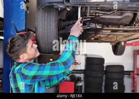 Portrait of mechanic repairing with a wrench a lifted car . Stock Photo