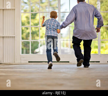 Young boy and his grandfather holding hands while skipping together inside a garage. Stock Photo