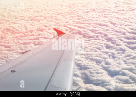 Plane flying over clouds at dawn. Airplane wing over beautiful cloudscape during dramatic colorful sunset or sunrise. Travel and vacation concept Stock Photo
