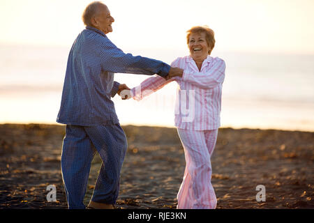 Happy senior couple dancing together at sunset on a beach in their pajamas. Stock Photo