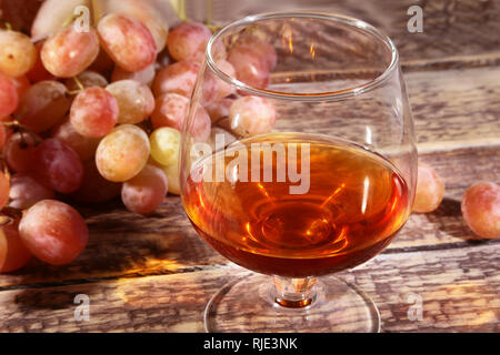 Glass with Cognac or Brandy and fresh grapes. still life in rustic style, vintage wooden background, selective focus. Stock Photo