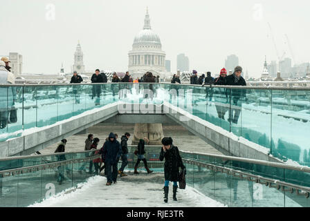 The Millenium Bridge covered in snow with St Pauls Cathedral in the background seen through falling snow; people making their way across the bridge. Stock Photo